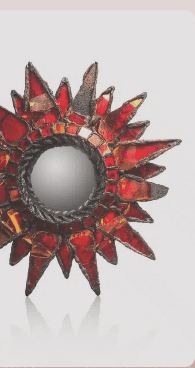 “Decoratieve spiegel in de vorm van de zon met stukjes rood gekleurd glas en een zwart metalen frame”